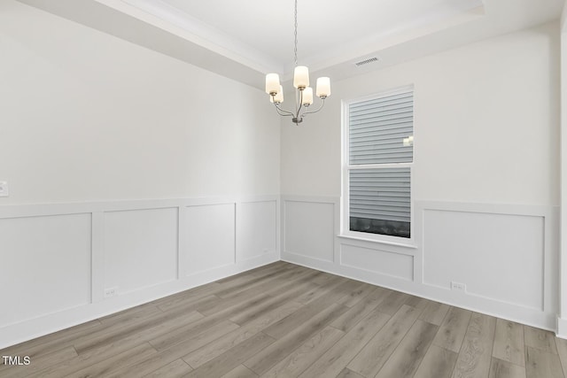 unfurnished room featuring a raised ceiling, a chandelier, and light hardwood / wood-style flooring