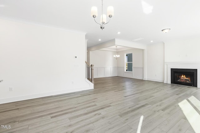 unfurnished living room featuring an inviting chandelier, ornamental molding, and light hardwood / wood-style flooring