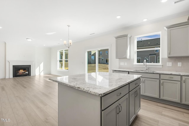 kitchen featuring sink, a center island, light wood-type flooring, hanging light fixtures, and gray cabinets