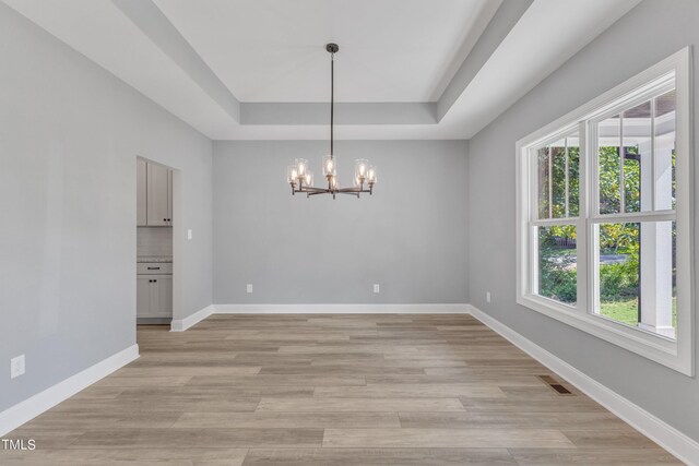 empty room with a raised ceiling, light wood-type flooring, and a chandelier