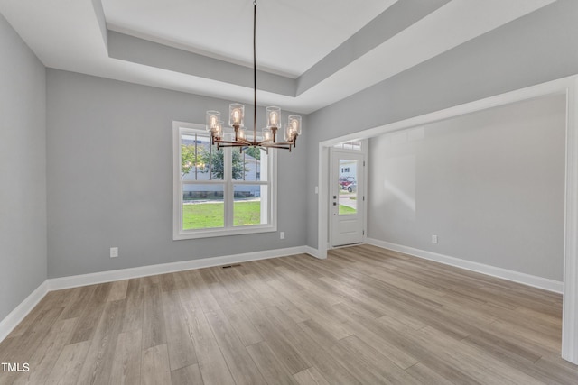 unfurnished dining area featuring a raised ceiling, an inviting chandelier, and light hardwood / wood-style flooring