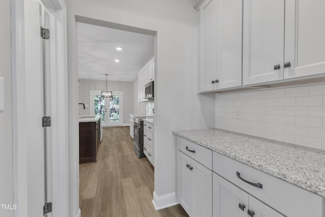 kitchen with appliances with stainless steel finishes, white cabinetry, light stone counters, light hardwood / wood-style floors, and decorative light fixtures