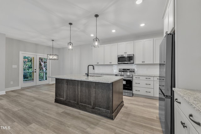 kitchen featuring white cabinetry, decorative light fixtures, an island with sink, stainless steel appliances, and light stone countertops