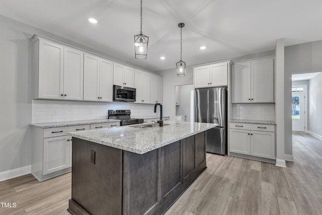 kitchen with appliances with stainless steel finishes, white cabinetry, sink, hanging light fixtures, and a kitchen island with sink