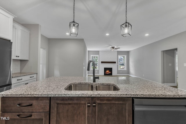 kitchen featuring sink, a fireplace, an island with sink, white cabinets, and decorative light fixtures