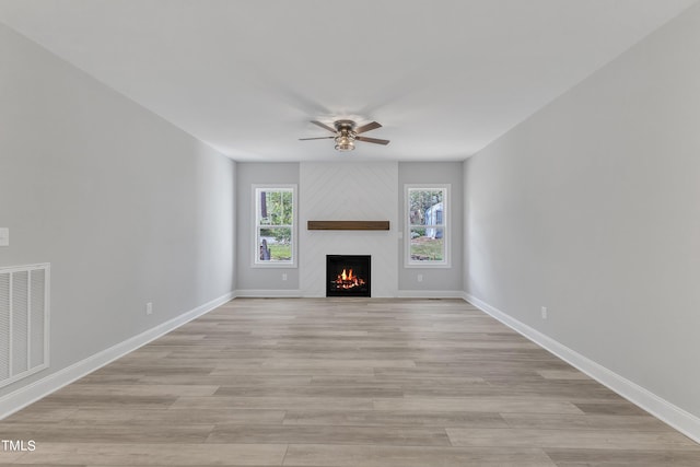 unfurnished living room featuring ceiling fan, a large fireplace, and light hardwood / wood-style floors