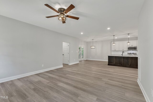 unfurnished living room with ceiling fan, sink, and light hardwood / wood-style flooring