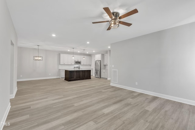 unfurnished living room with ceiling fan with notable chandelier and light hardwood / wood-style floors