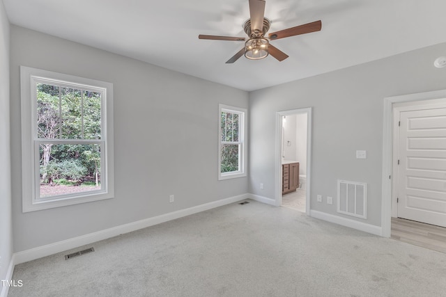 unfurnished bedroom featuring multiple windows, connected bathroom, light carpet, and ceiling fan