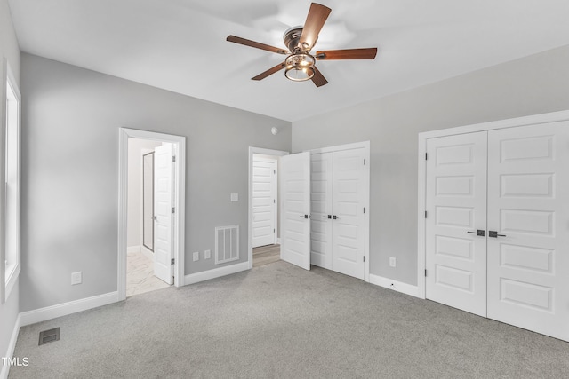 unfurnished bedroom with light carpet, multiple closets, and ceiling fan