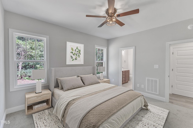 bedroom featuring multiple windows, ensuite bathroom, light carpet, and ceiling fan