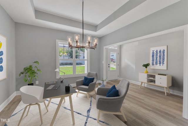 home office with a tray ceiling, light hardwood / wood-style flooring, and a chandelier