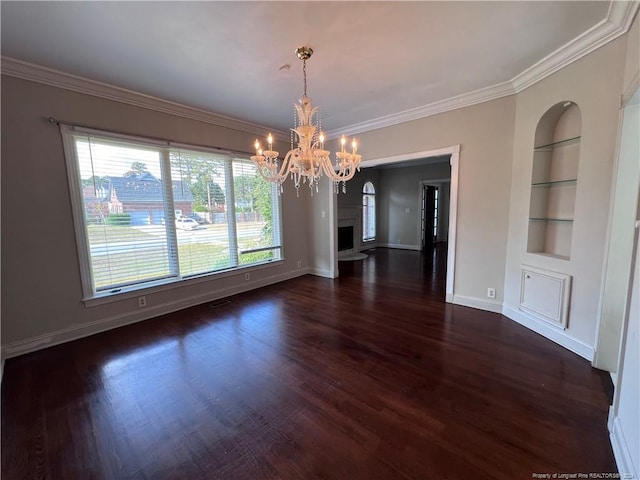 unfurnished dining area featuring dark wood-type flooring, ornamental molding, built in shelves, a chandelier, and a fireplace