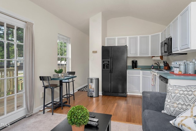 kitchen featuring white cabinets, light hardwood / wood-style floors, vaulted ceiling, and black appliances