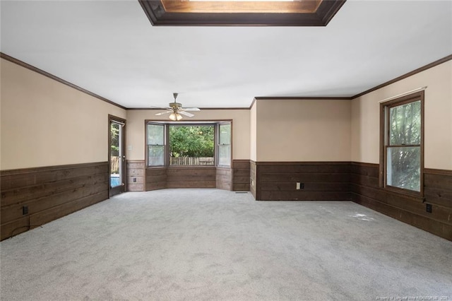 carpeted empty room with ceiling fan, wood walls, and ornamental molding