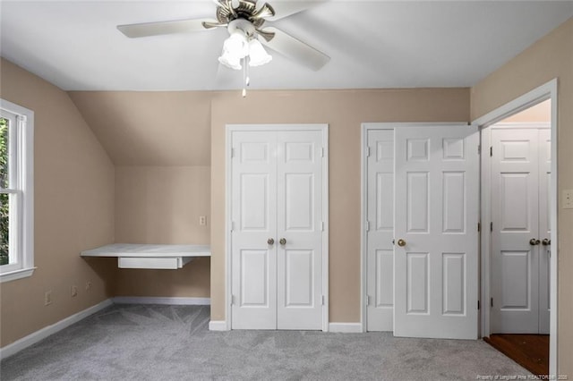 unfurnished bedroom with ceiling fan, vaulted ceiling, light colored carpet, and multiple closets