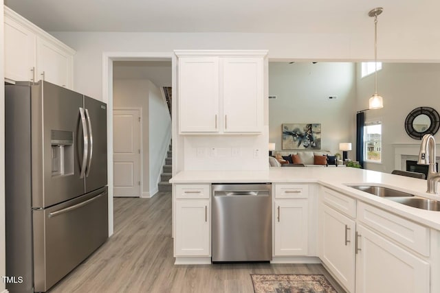 kitchen with sink, light hardwood / wood-style flooring, hanging light fixtures, appliances with stainless steel finishes, and white cabinets