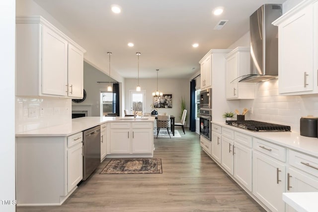 kitchen with decorative light fixtures, white cabinetry, kitchen peninsula, stainless steel appliances, and wall chimney exhaust hood