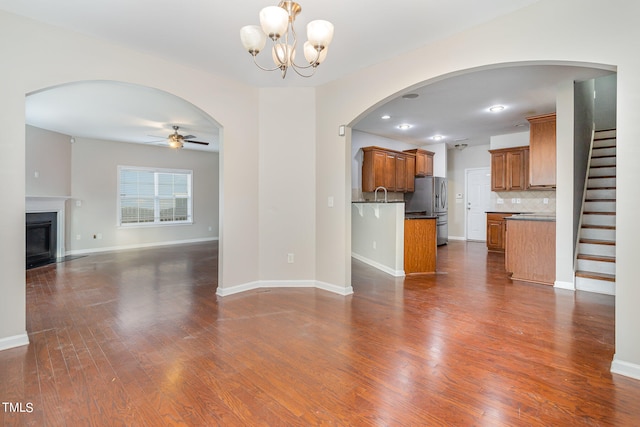 unfurnished living room featuring sink, ceiling fan with notable chandelier, and dark hardwood / wood-style flooring