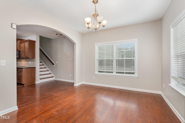 empty room with dark wood-type flooring, plenty of natural light, and a notable chandelier