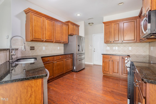 kitchen featuring backsplash, appliances with stainless steel finishes, dark wood-type flooring, sink, and dark stone counters