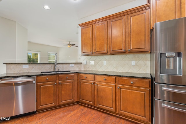 kitchen with stainless steel appliances, sink, hardwood / wood-style floors, and dark stone counters