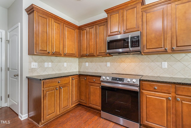 kitchen with stainless steel appliances, dark stone countertops, backsplash, and dark hardwood / wood-style flooring