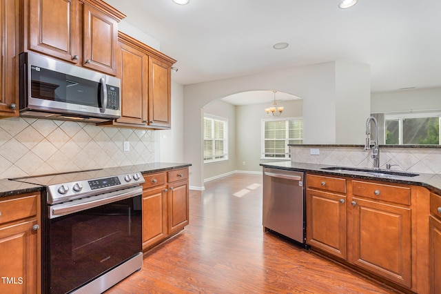 kitchen with stainless steel appliances, light hardwood / wood-style floors, a notable chandelier, sink, and dark stone counters