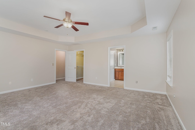 unfurnished bedroom featuring ensuite bathroom, a walk in closet, a closet, a raised ceiling, and ceiling fan