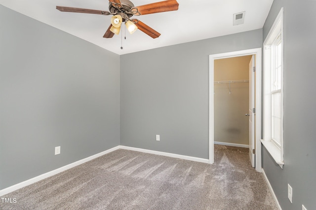 unfurnished bedroom featuring ceiling fan, a walk in closet, a closet, and carpet floors