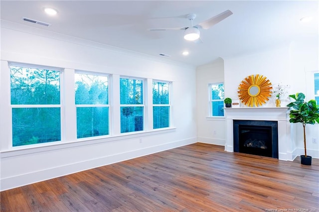 unfurnished living room featuring ceiling fan, wood-type flooring, ornamental molding, and a wealth of natural light