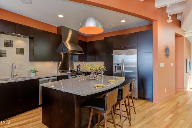 kitchen with light stone counters, wall chimney exhaust hood, backsplash, light wood-type flooring, and sink