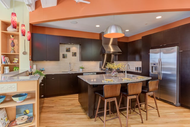 kitchen with light hardwood / wood-style floors, backsplash, light stone counters, stainless steel fridge, and wall chimney exhaust hood