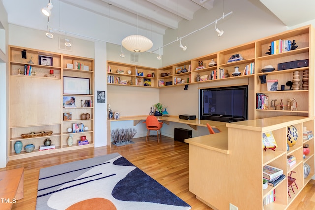 living room featuring beamed ceiling, track lighting, built in desk, and light hardwood / wood-style floors