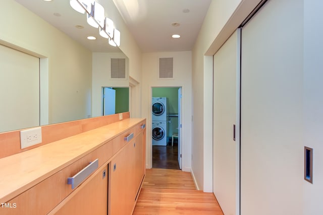 hall with stacked washer and clothes dryer and light hardwood / wood-style floors