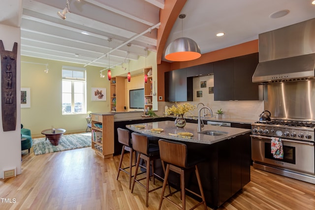 kitchen with decorative backsplash, light hardwood / wood-style flooring, an island with sink, and range with two ovens