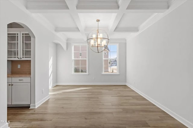 unfurnished dining area with coffered ceiling, baseboards, light wood-type flooring, beam ceiling, and an inviting chandelier