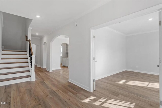 unfurnished room with arched walkways, ornamental molding, wood finished floors, and baseboards