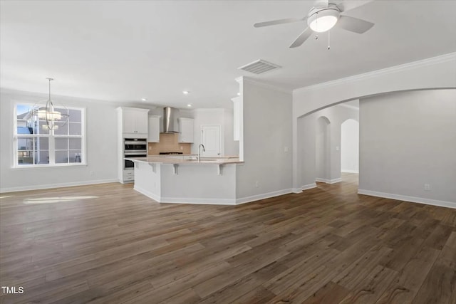 unfurnished living room with visible vents, arched walkways, wood finished floors, crown molding, and ceiling fan with notable chandelier