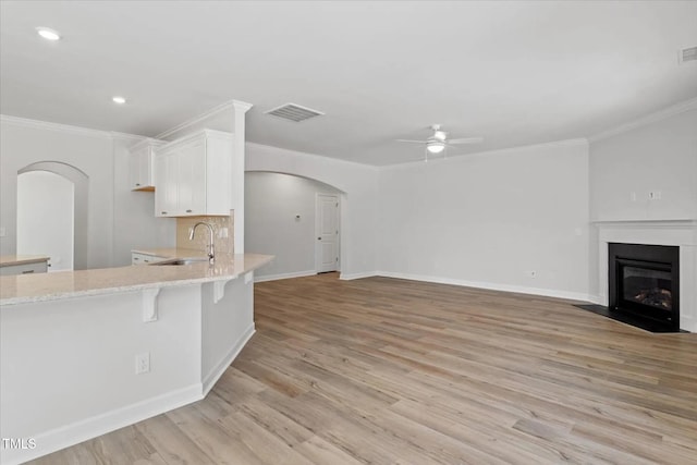 kitchen featuring arched walkways, a fireplace with flush hearth, white cabinetry, a sink, and light wood-type flooring