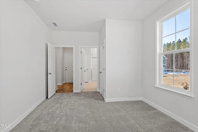 unfurnished bedroom featuring multiple windows, carpet, visible vents, and baseboards