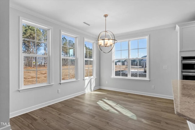 unfurnished dining area featuring dark wood-style floors, a healthy amount of sunlight, crown molding, and a notable chandelier