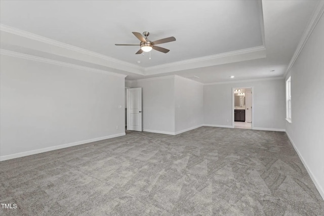 spare room with a tray ceiling, a ceiling fan, ornamental molding, carpet flooring, and baseboards