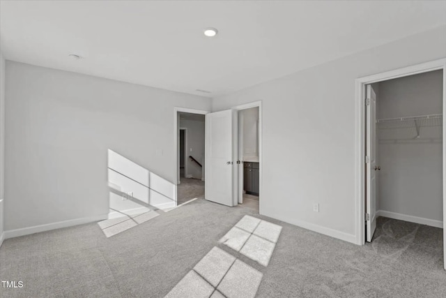 unfurnished bedroom with baseboards, a walk in closet, a closet, and light colored carpet