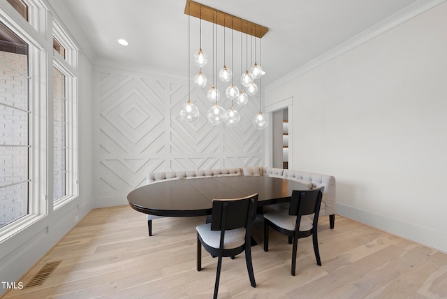 dining area with ornamental molding, an inviting chandelier, and light hardwood / wood-style floors