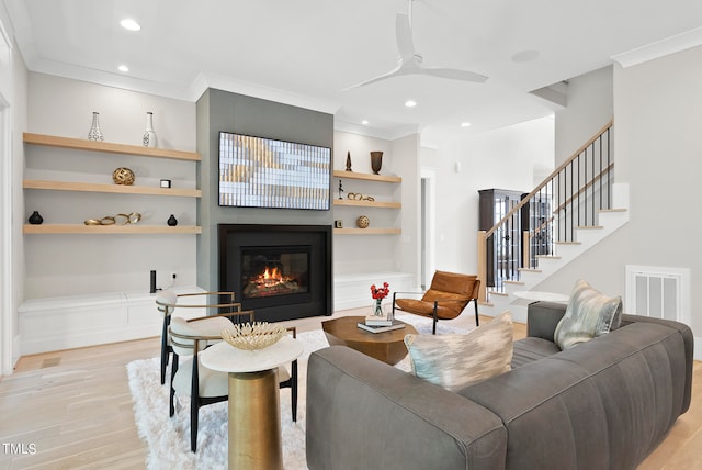 living room with built in shelves, crown molding, ceiling fan, and light hardwood / wood-style floors