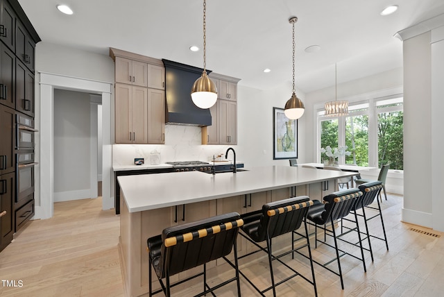 kitchen with a center island with sink, backsplash, premium range hood, light hardwood / wood-style flooring, and sink