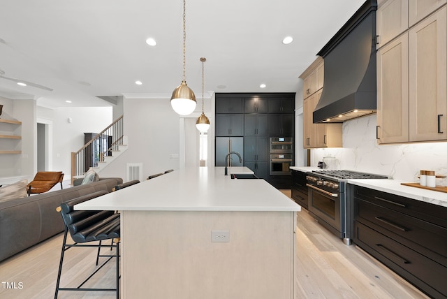 kitchen featuring light brown cabinetry, custom range hood, a kitchen island with sink, tasteful backsplash, and high end appliances