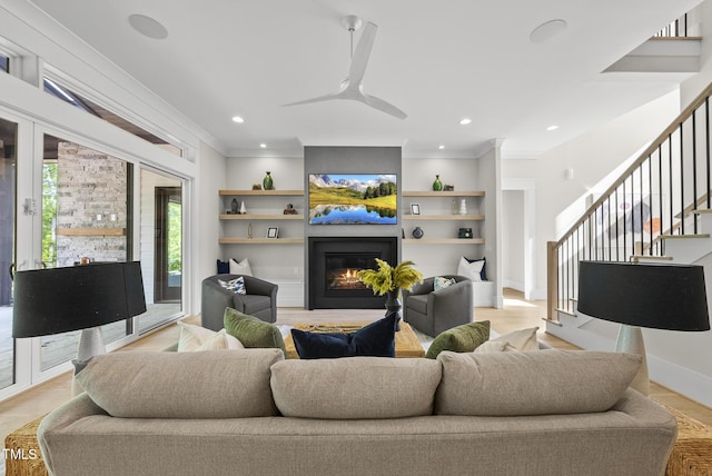living room with built in shelves, a glass covered fireplace, crown molding, and stairs