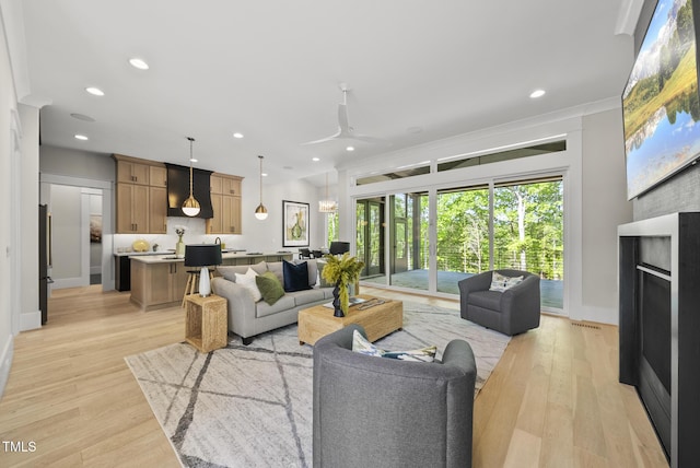 living room with light wood-style floors, ceiling fan, baseboards, ornamental molding, and recessed lighting
